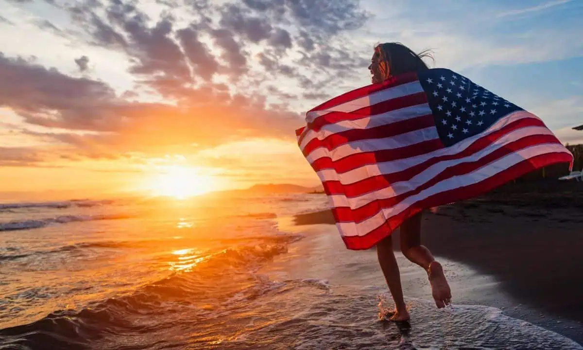 Young girl running down the beach with an American flag
