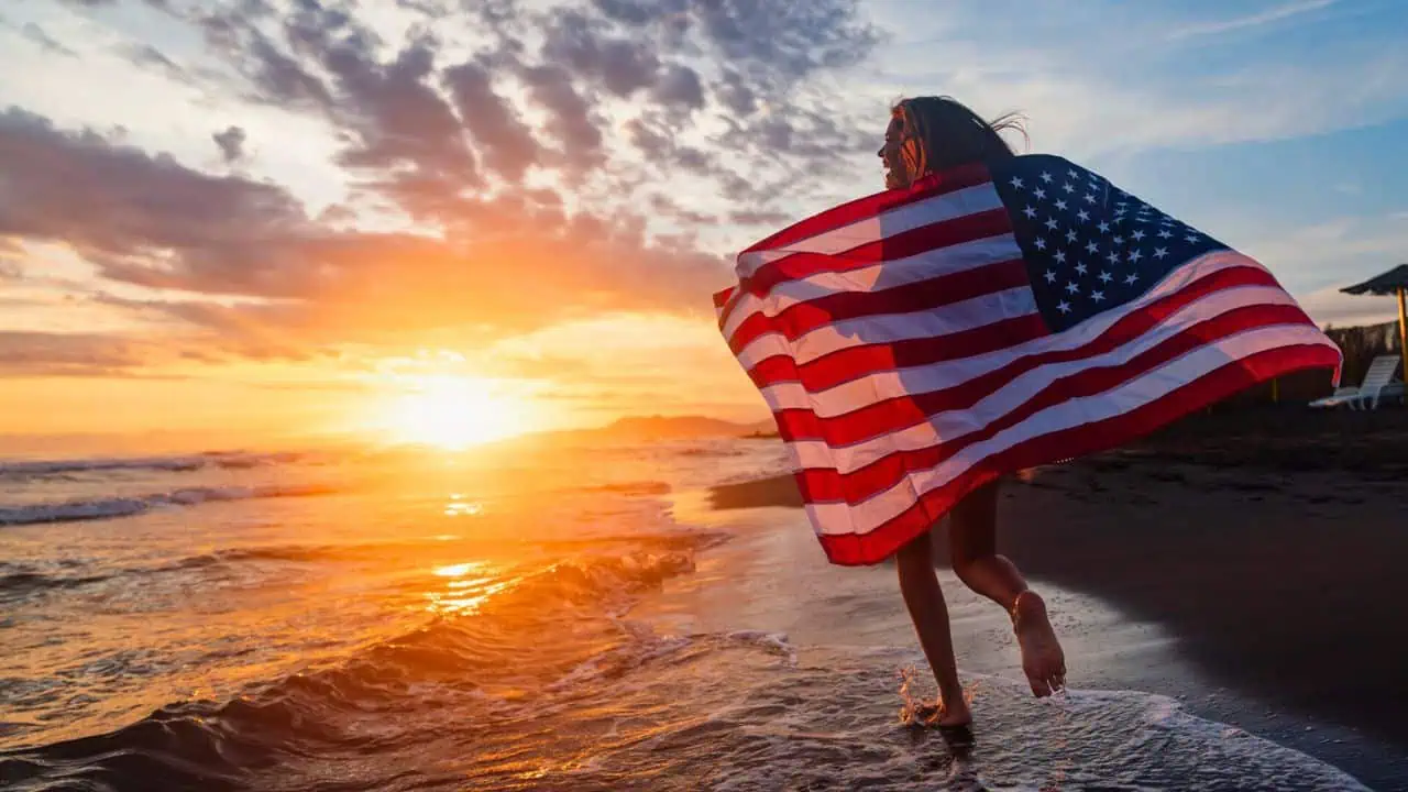 Young girl running down the beach with an American flag