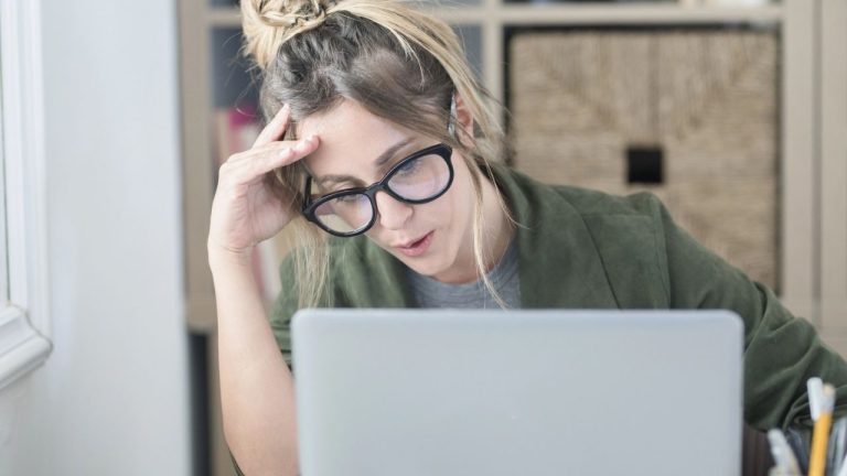 Woman looking concerned while checking travel prices on laptop at home